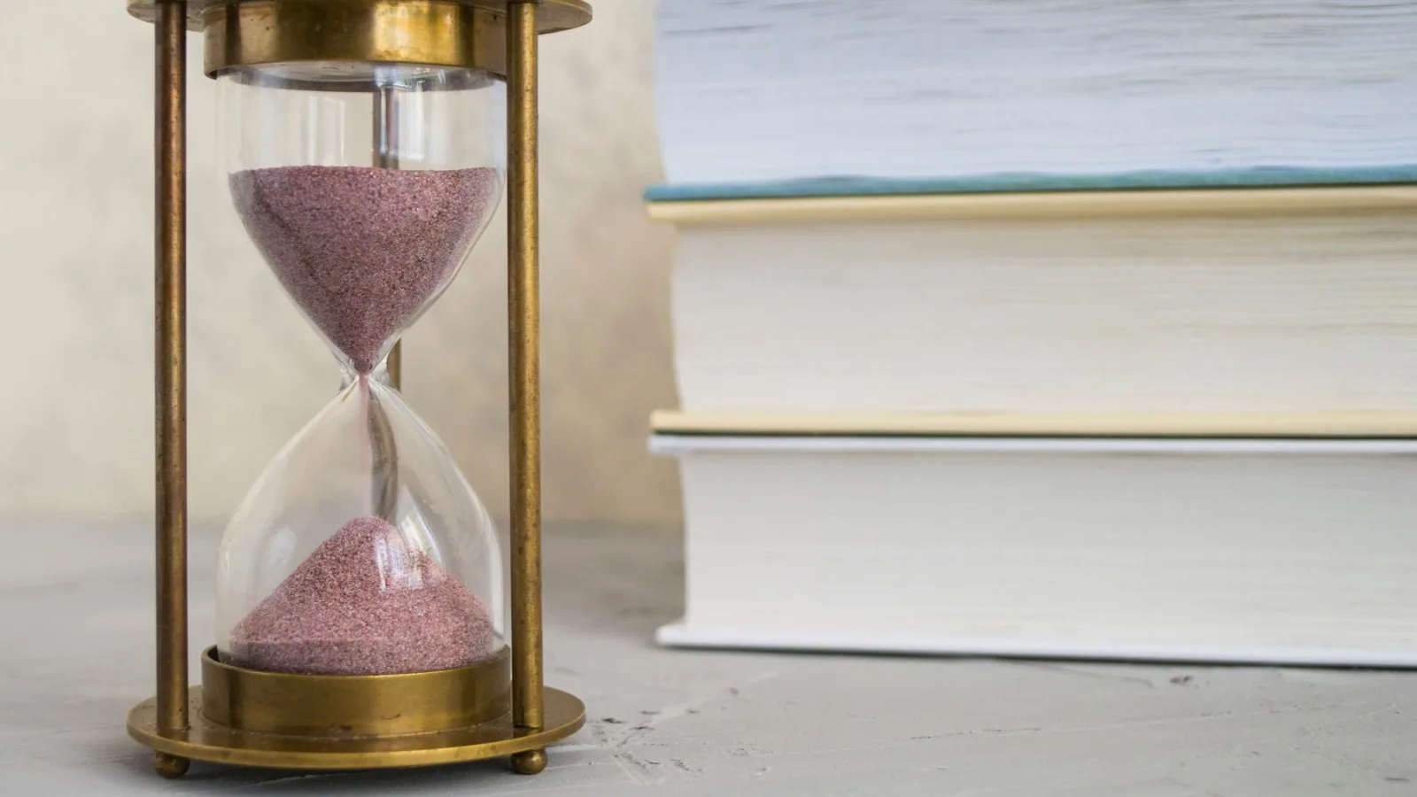 Brass hourglass with pink sand running, beside a stack of books