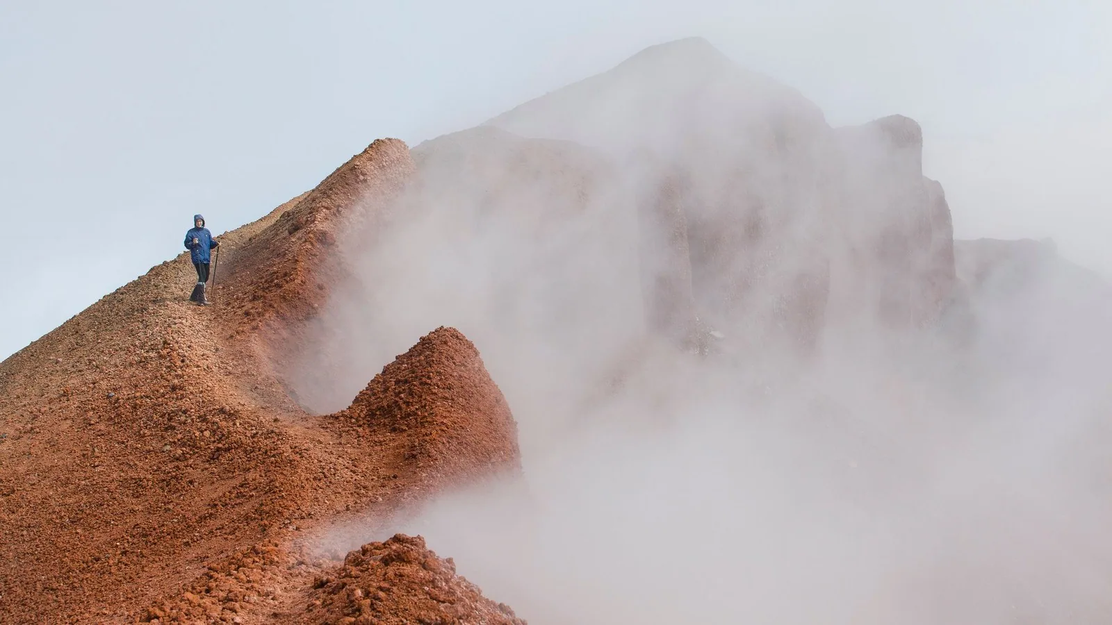 A lone hiker climbing a red rock ridge into thick mountain fog