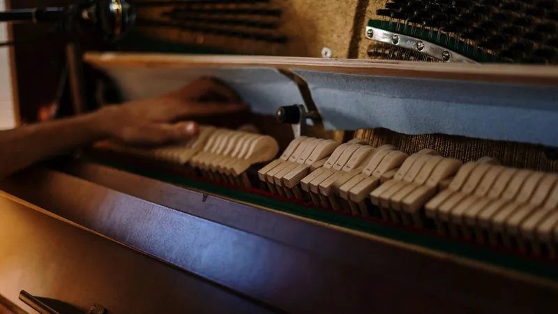 A hand adjusting the hammers inside an open upright piano during tuning