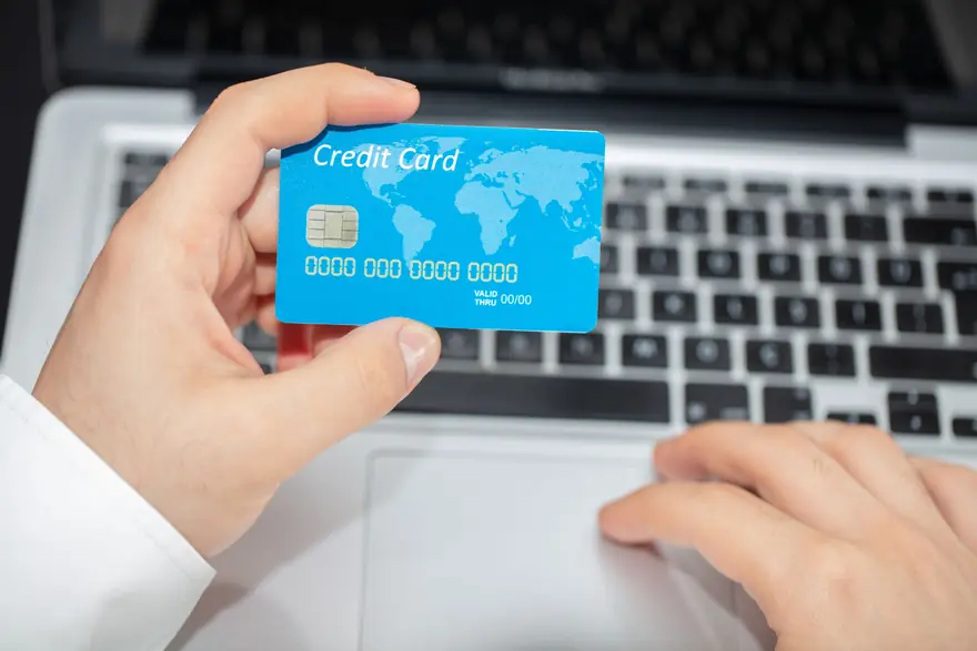 A hand holds a generic credit card above a laptop keyboard