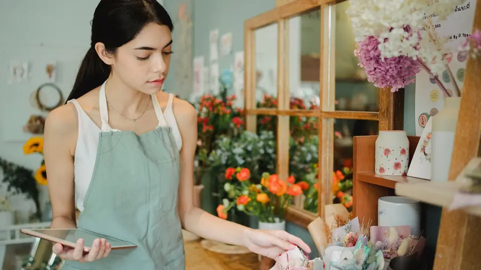 A florist checks a tablet while arranging bouquets in a flower shop
