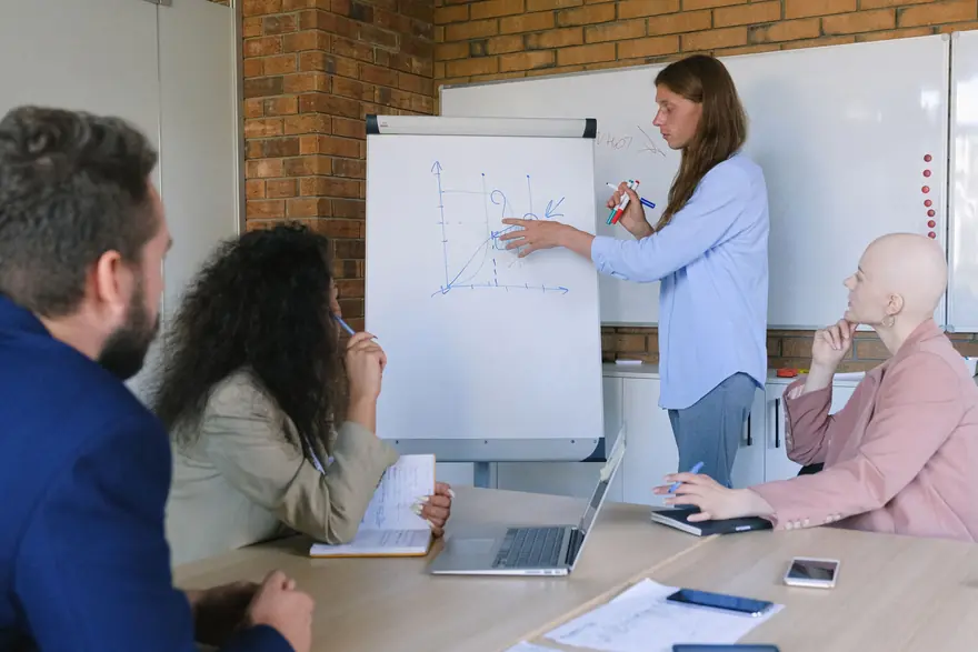 A colleague sketches a chart on a flip chart while teammates take notes