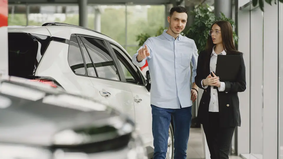 A salesperson walks a customer through a bright car showroom