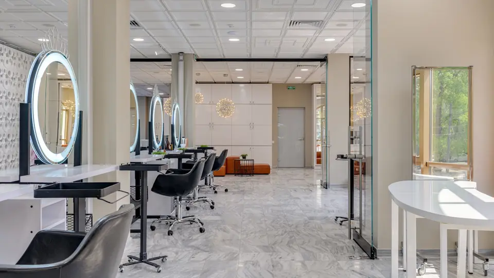 A bright beauty salon with round lit mirrors, styling chairs and a marble floor