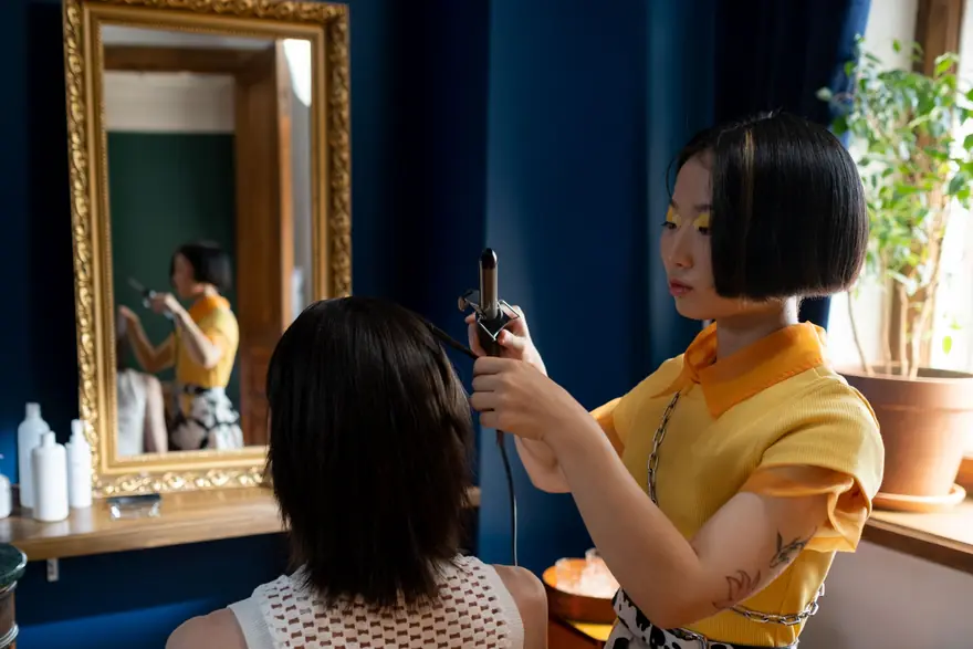A stylist curls a client's hair in front of a gold framed mirror