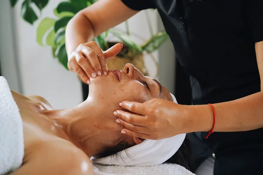 A therapist gives a client a facial massage in a treatment room