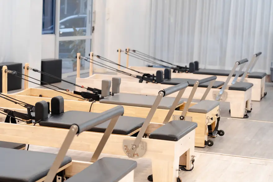 A row of wooden reformer machines in an empty pilates studio