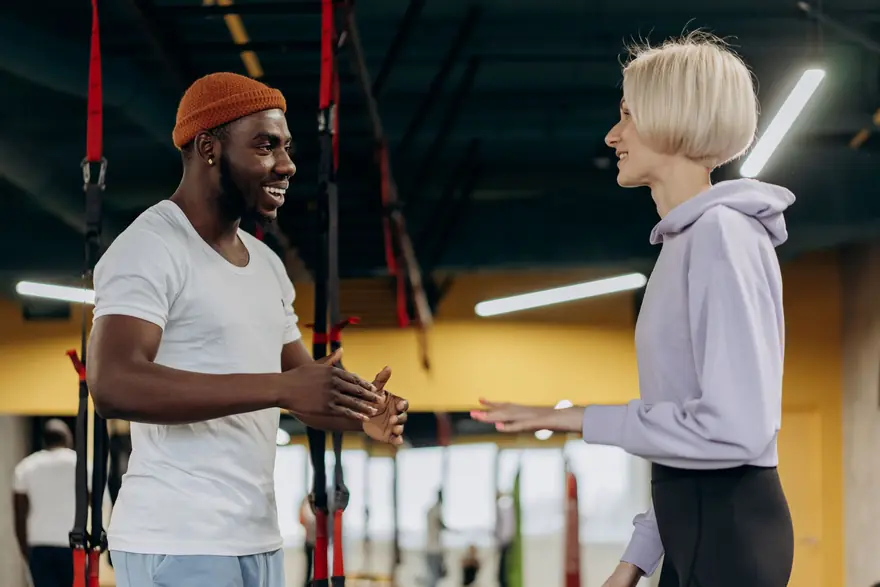 A trainer and a client talk and laugh in a gym