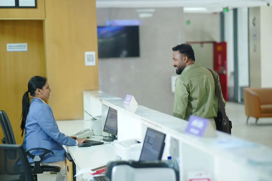 A receptionist at a long hospital front desk as a visitor walks in