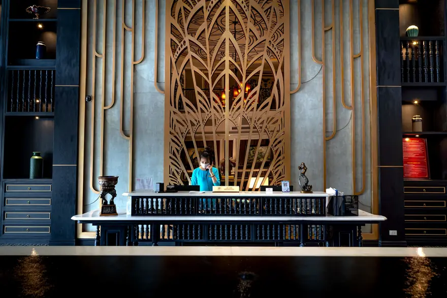 A receptionist works behind a grand carved wooden front desk in a hotel lobby
