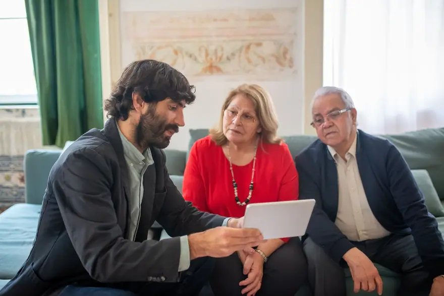 An adviser shows an older couple something on a tablet as they sit on a sofa