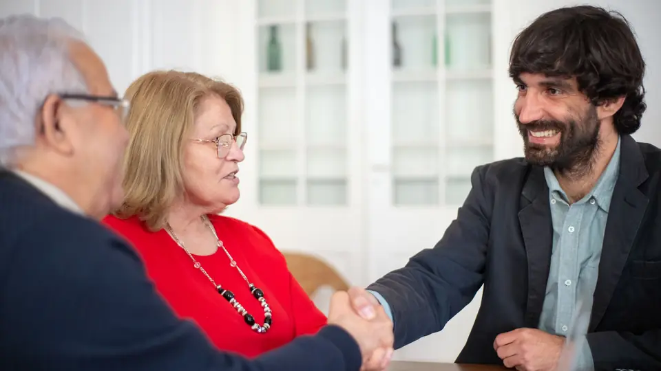 An adviser shakes hands with an older couple across a desk