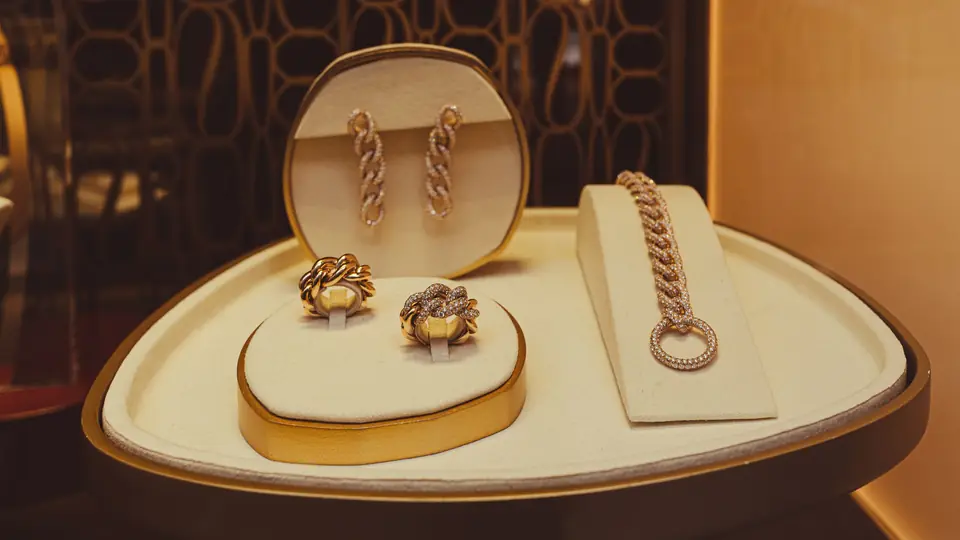 Gold rings, earrings and a bracelet displayed on cream stands under warm light