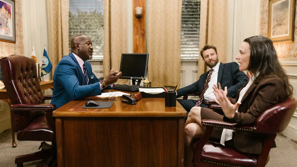 Two clients talk with a lawyer across a wooden desk in a traditional panelled office