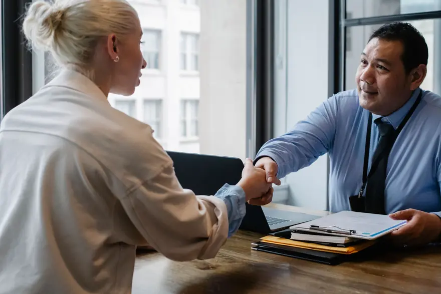 A consultant shakes hands with a client across a desk with folders