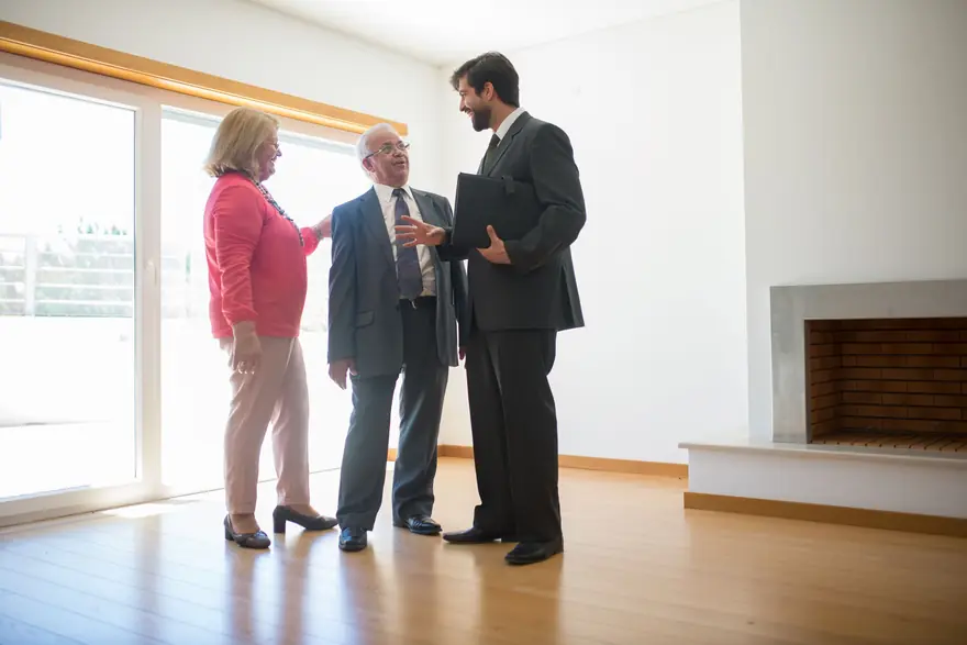 An agent in a suit shows an older couple around a bright empty apartment