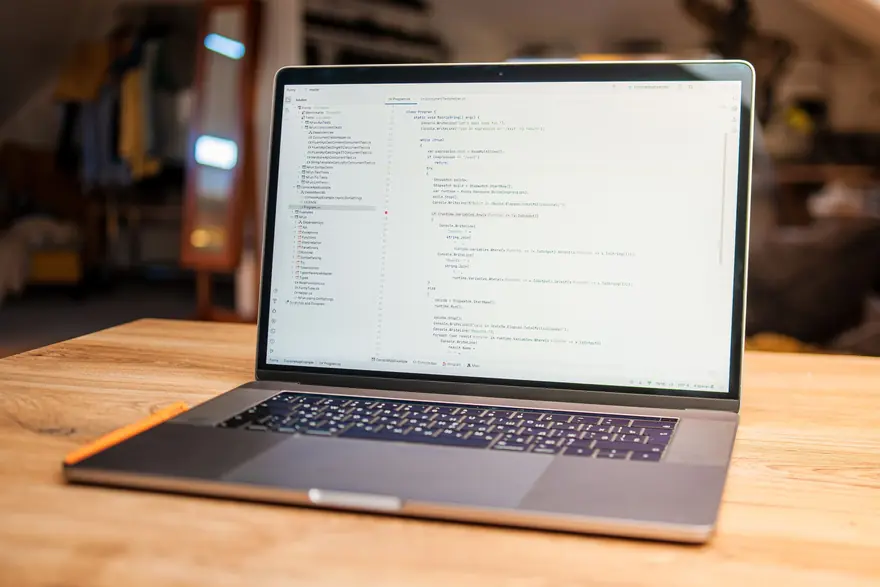 A laptop showing code sits open on a wooden desk