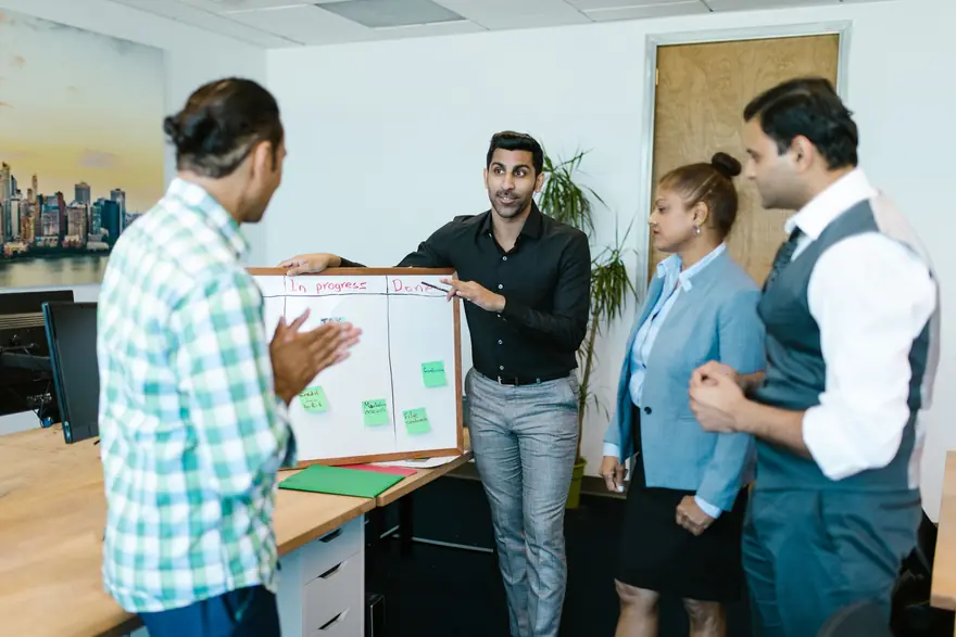 A team stands around a small board on a desk, planning a project