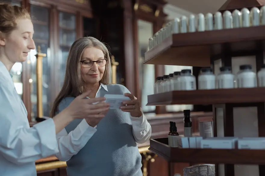 A shop assistant shows a product box to a smiling older customer beside wooden shelves