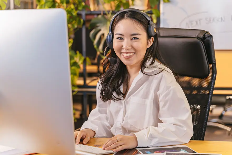 A smiling woman with a headset sits at a desk with a computer