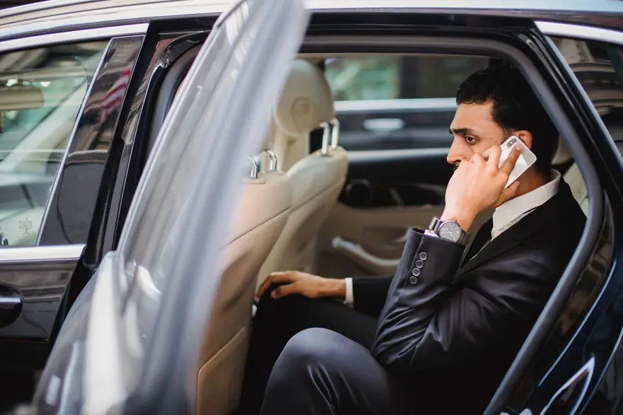 A man in a suit talks on his phone in the back seat of a car