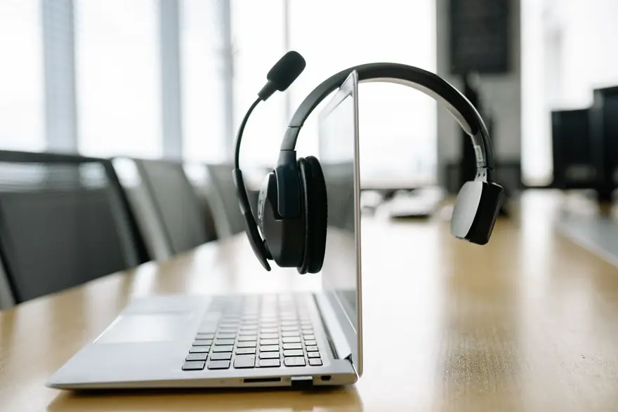 A headset hangs over the screen of an open laptop on a meeting table