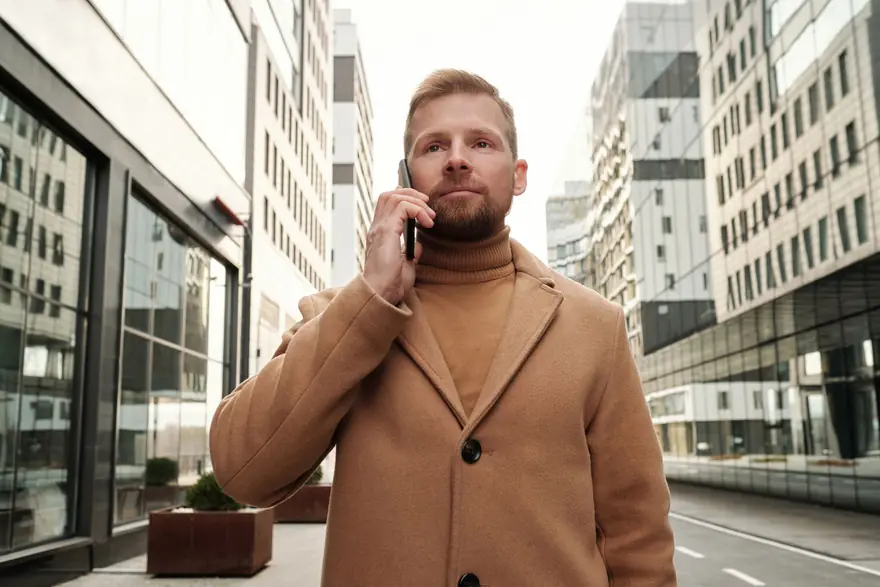 A man in a camel coat takes a phone call on a city street