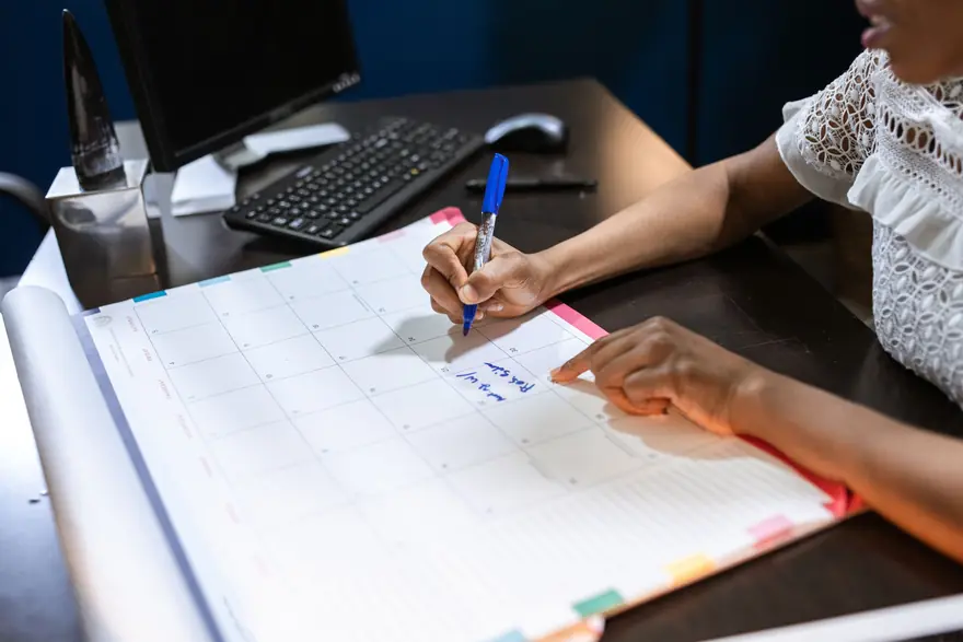 A hand writes appointments into a large desk planner