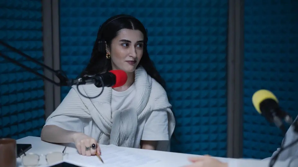 A woman at a studio desk with a microphone and printed notes
