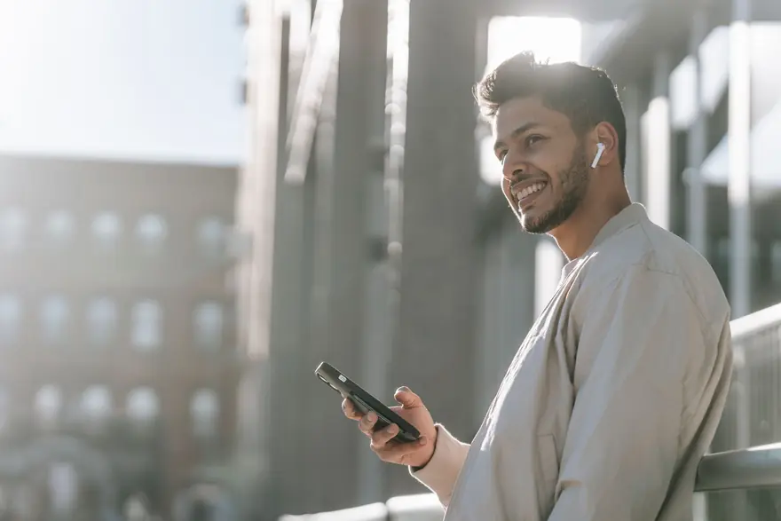 A man with a wireless earbud smiles as he plays a message on his phone