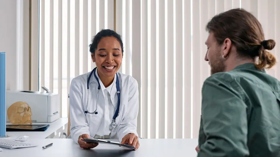 A smiling doctor talks with a patient across a consultation desk