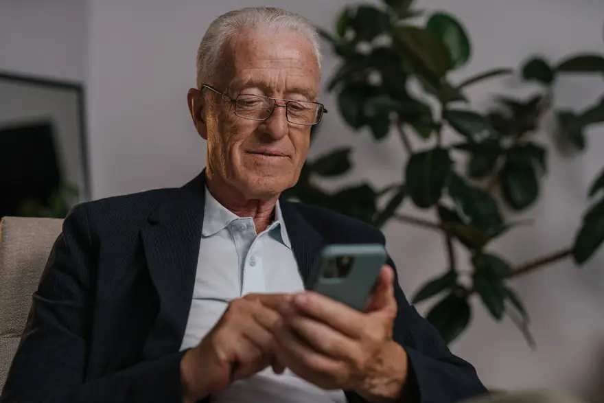 An older man in a jacket reads something on his phone