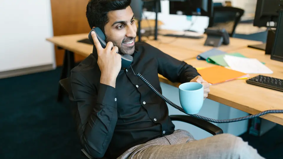 A smiling salesman leans back at his desk on a phone call