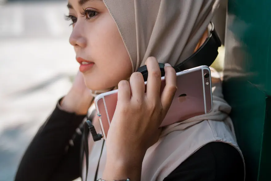 A woman in a headscarf holds her phone to her ear to listen