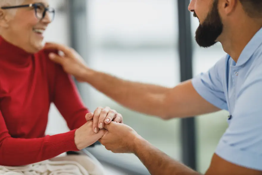 A clinician holding an older patient's hands as she laughs