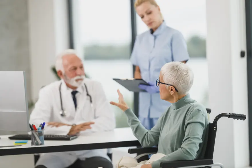 A doctor and a nurse talking with an older patient at the consultation desk
