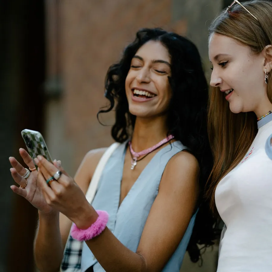 Two friends laughing at a phone in the street