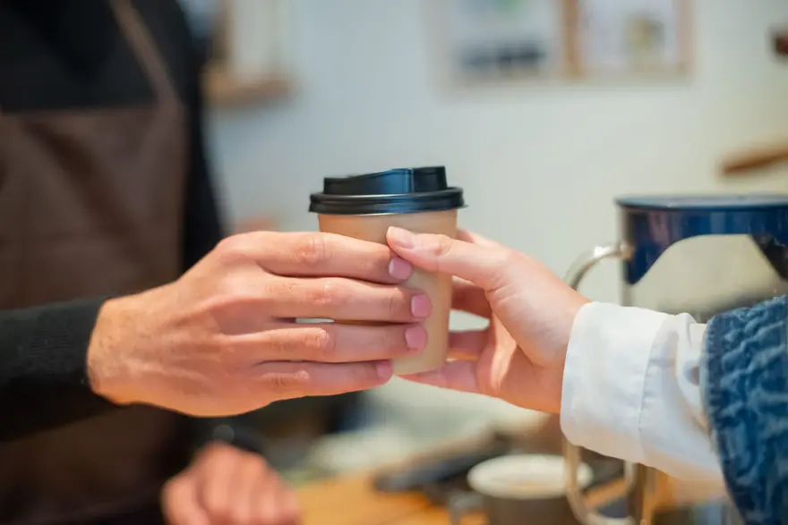 One person passes a takeaway coffee cup to another
