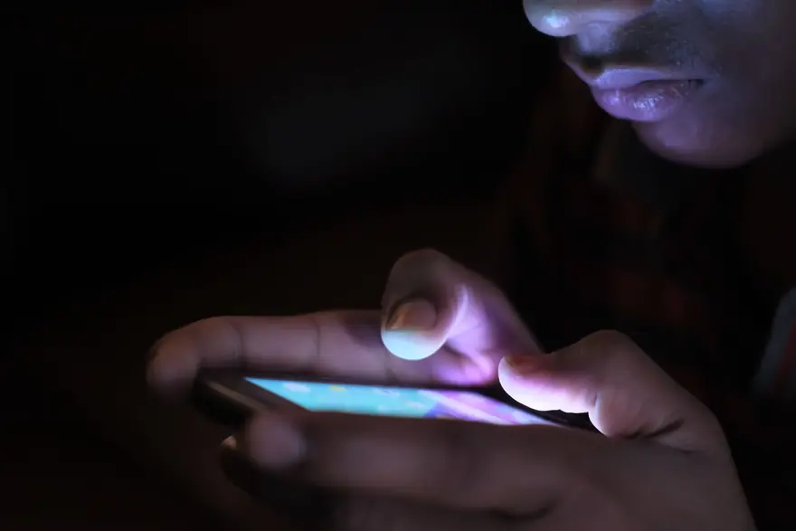 A face lit only by a phone screen in the dark as the person types