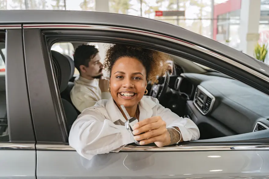 A smiling driver holds up a car key from the driver's seat