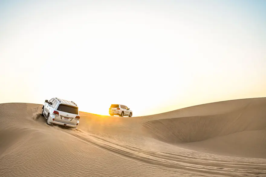 Two four-wheel-drive vehicles crossing sand dunes on a desert drive at sunset