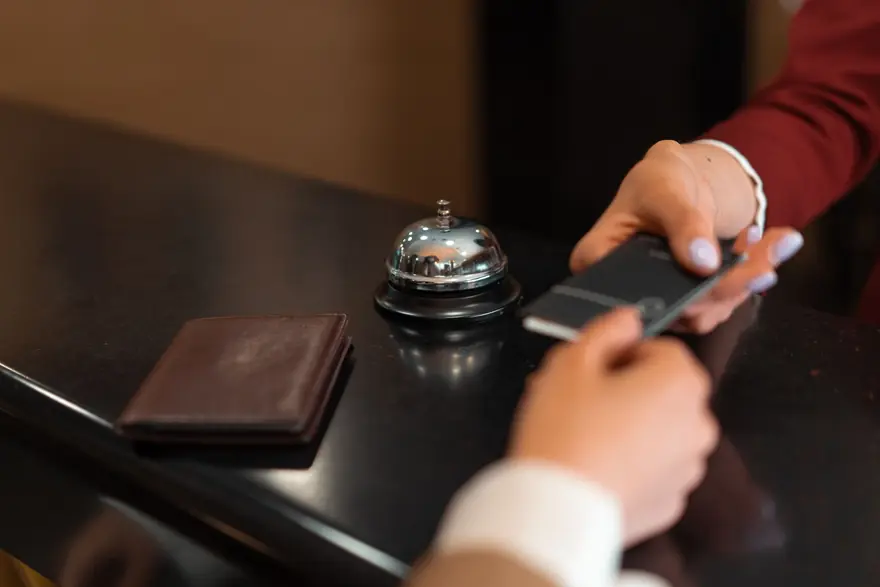 A card being handed across a hotel front desk beside a service bell