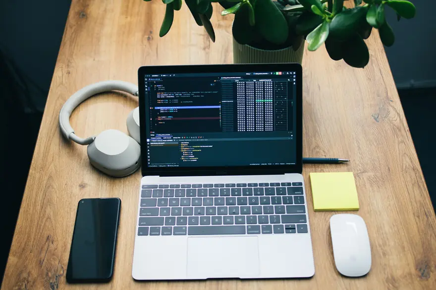 A laptop, a phone and a pair of headphones laid out on a wooden desk