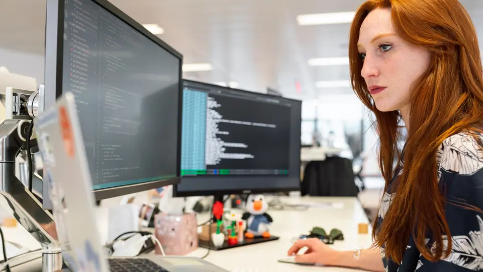 A developer works at a desk with code open on two monitors