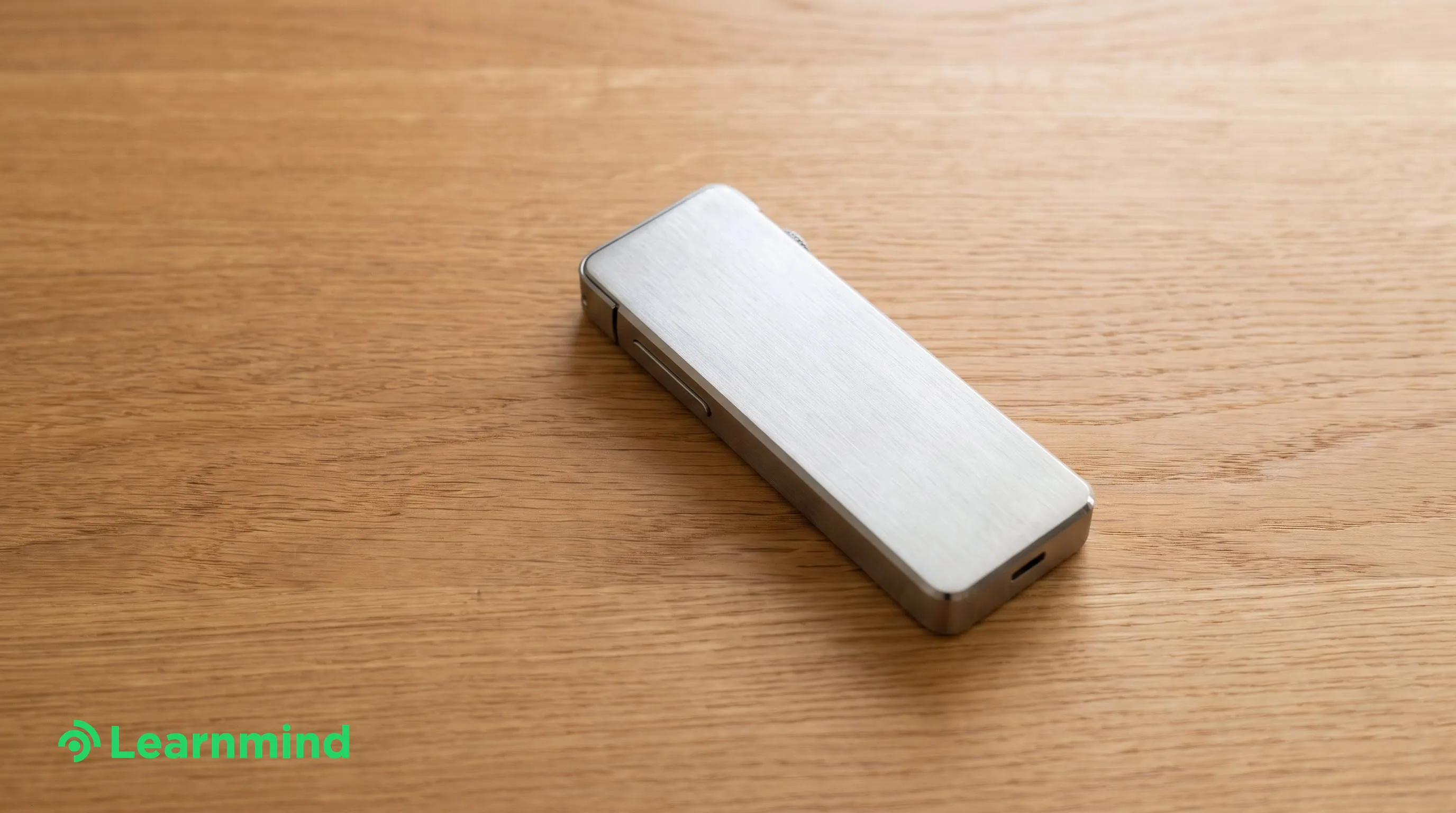 Brushed metal recorder device on warm wood desk, bright daylight